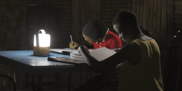 Deux écoliers font leurs devoirs avec la lanterne Access To Energy Solutions.
